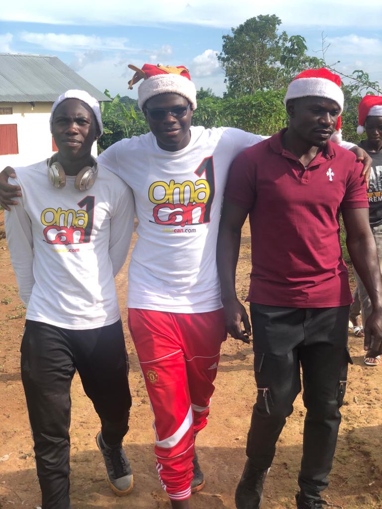 Three young men in Omacan t-shirts and Santa hats walk arm in arm
