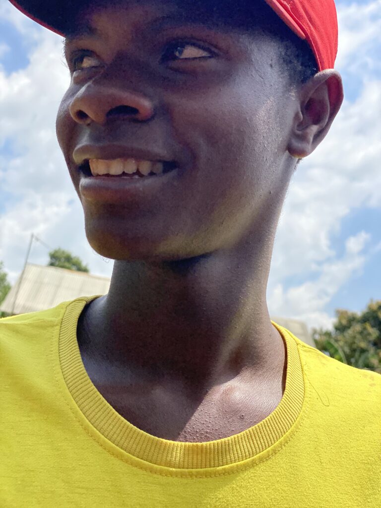 A young man in a yellow shirt and red baseball cap smiles